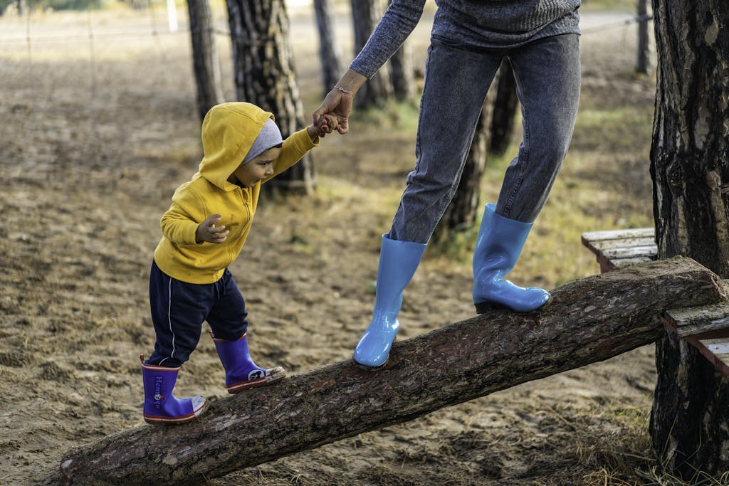 A woman helps her toddler walk on a log in a park, showcasing child support and family bonding.