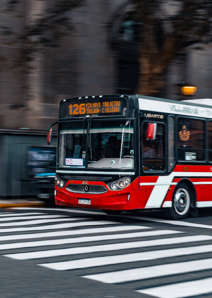 Dynamic capture of a red city bus crossing a street in an urban setting.