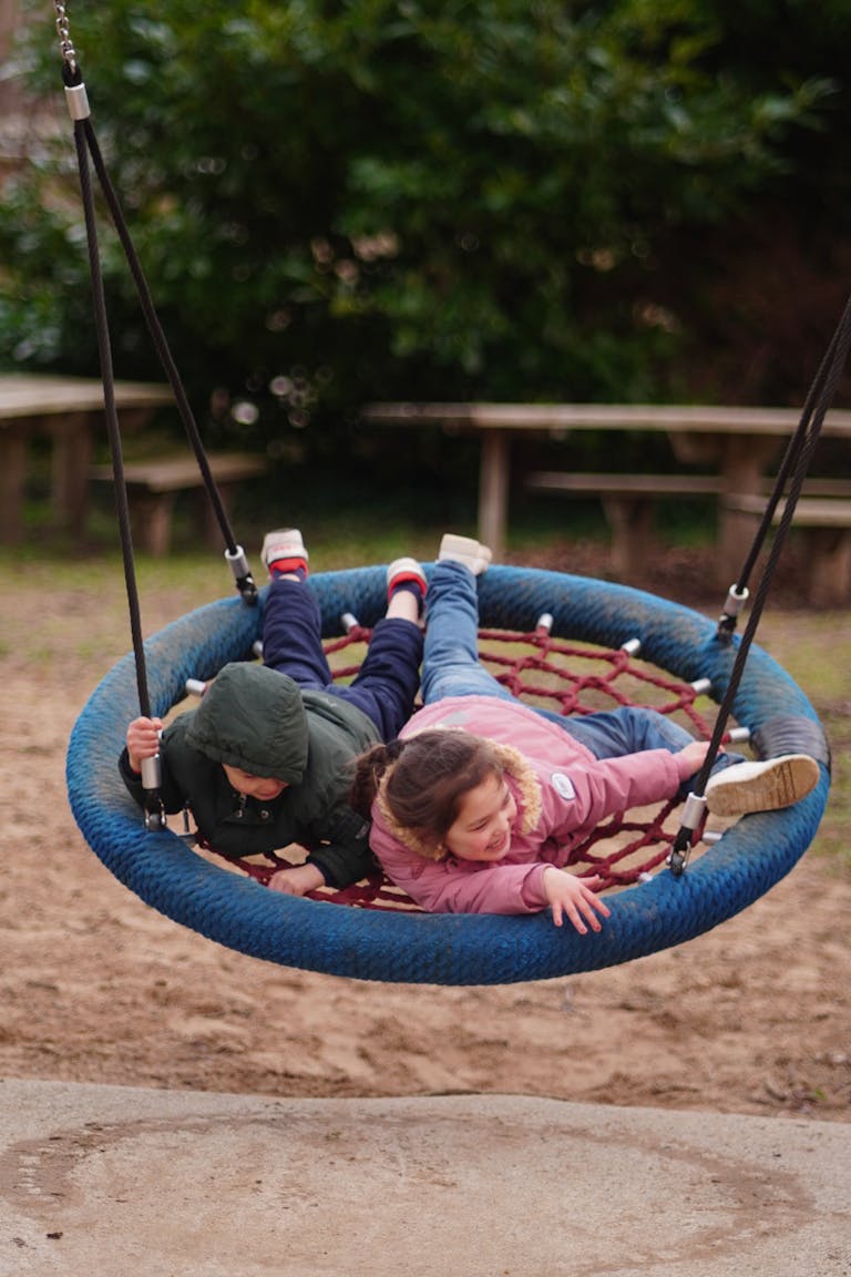 Two children happily playing on a round swing in a park setting, capturing the essence of outdoor fun.